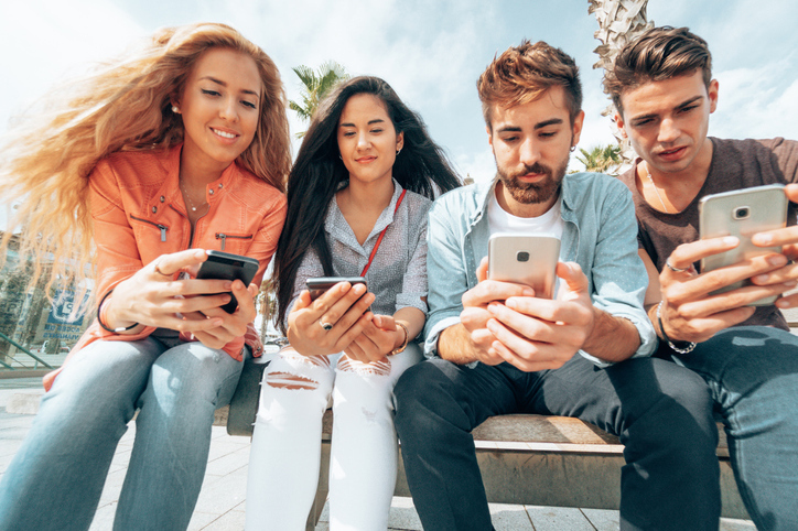 A group of 4 teenagers sat down scrolling social media on their mobile phone